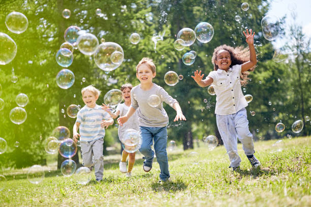 Multi-ethnic group of little kids with toothy smiles on their faces enjoying warm sunny day while participating in soap bubbles show