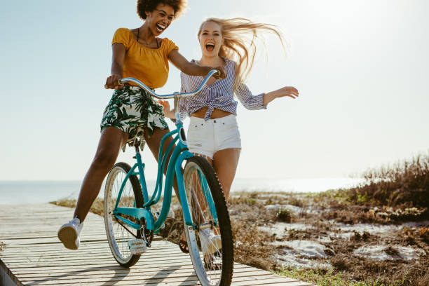 Cheerful female having fun with a cycle outdoors. Two girls playing with a bicycle on the boardwalk on seaside.