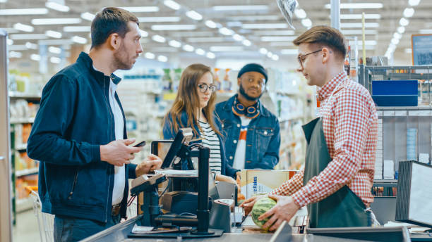 At the Supermarket: Checkout Counter Customer Pays with Smartphone for His Item with Friendly Cashier, Small Lines and Modern Wireless Paying Terminal System at fenton mi 48430.