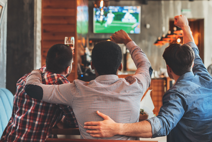 Three men watching football on TV in sport bar, back view