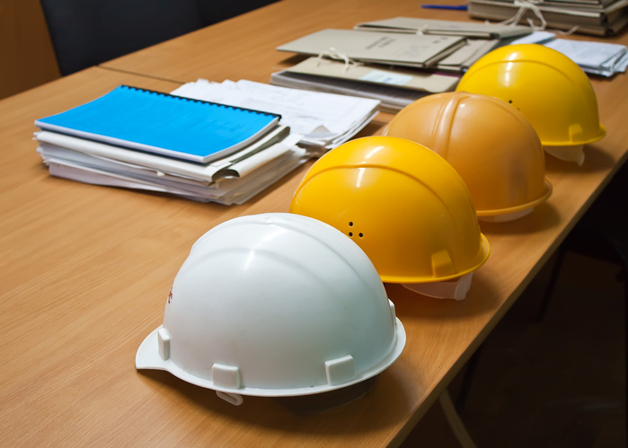 Four hard hats on a wooden desk next to documents