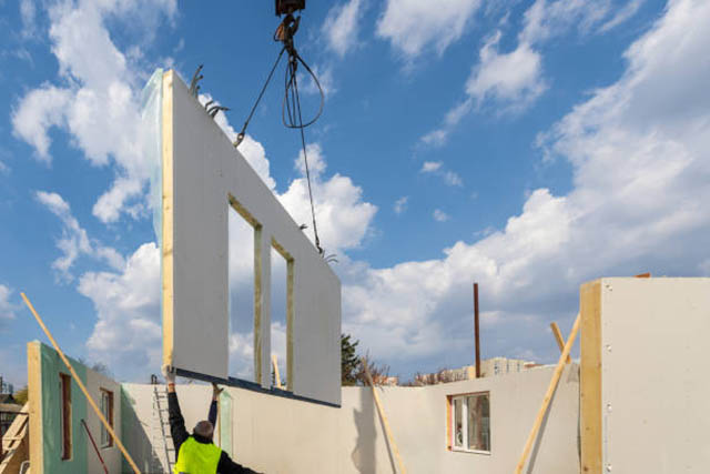 Construction new and modern modular house from composite sip panels. Worker man in uniform wear working on building development industry of energy efficient property against blue sky background