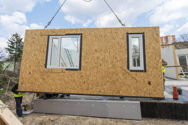 Process of construction new and modern modular house. Workman in special protective uniform wear standing behind sip panel and working on building development industry of energy efficient property