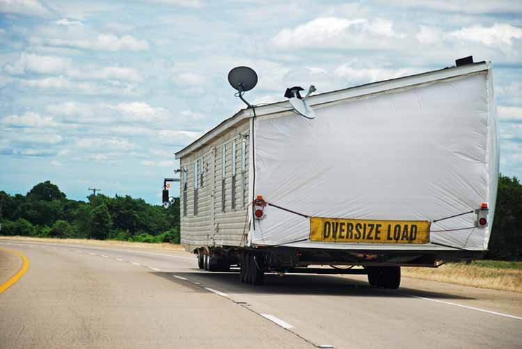 Half of double-wide house trailer being transported along interstate highway.