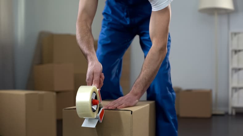 Moving company worker packing cardboard boxes, quality delivery services moving container