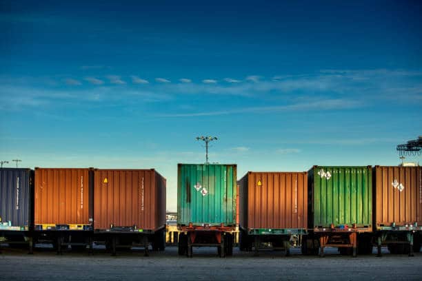 Rear view of a line of trucks loaded with differently colored shipping containers. moving container.